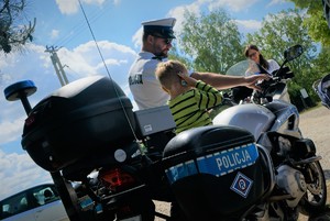 Na policyjnym motocyklu siedzi mały chłopiec, przy nim stoi policjant ruchu drogowego