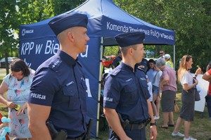 Dwaj policjanci w furażerkach stoją na tle profilaktycznego namiotu Komendy Powiatowej Policji w Bieruniu, przy którym znajdują się dzieci i dorośli